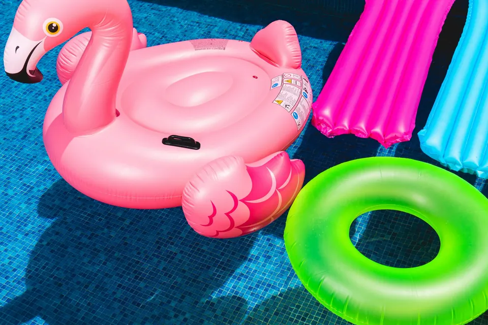 A pink flamingo float, pool noodles and a green ring floating in a pool